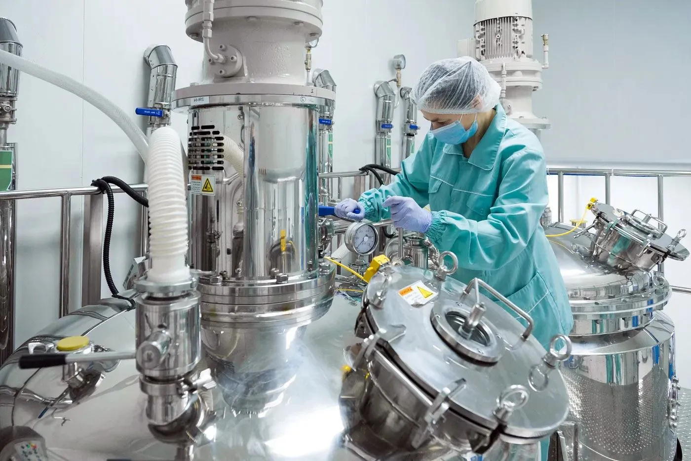 Production operator checking stainless-steel liquid supplement processing equipment